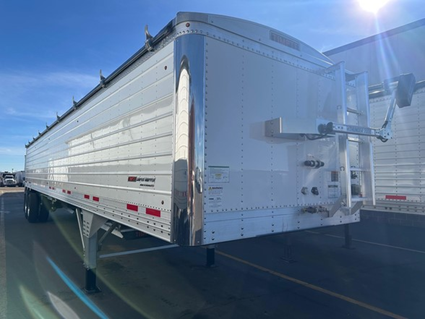 Trailer side view showing Timpte Super Hopper trailer with silver corrugated aluminum walls and front/gooseneck area; visible landing legs and wheel area.