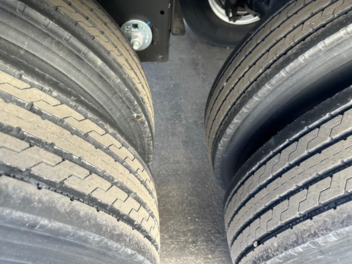 Trailer tires in a dual-axle configuration showing tread and sidewalls with a small portion of the suspension and frame.