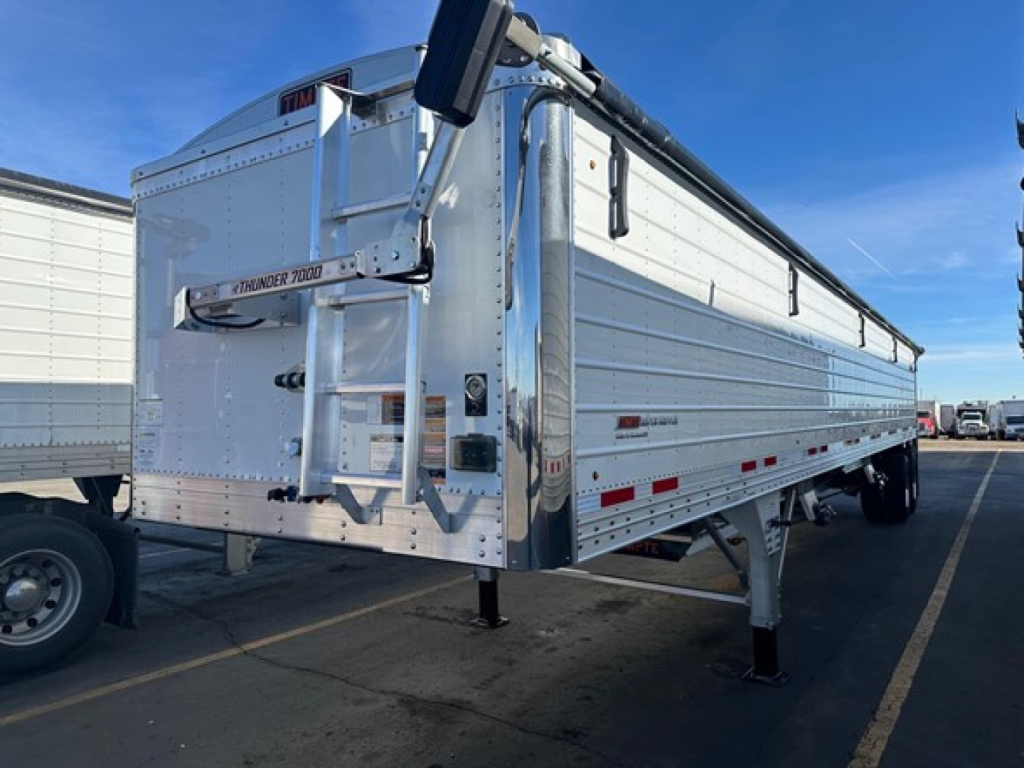 Trailer showing a white Timpte Super Hopper with fold-down ladder, hinged side panels, and landing legs visible in a parking lot.