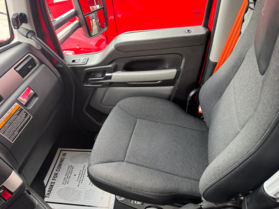 Kenworth T680 truck interior driver seat and door panel with gray fabric seat, black dashboard, red exterior visible through window.