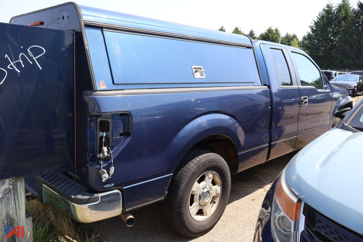Ford F-150 pickup truck with camper shell rear view showing side profile and spare tire, blue exterior, two-door crew cab style, tailgate area visible.