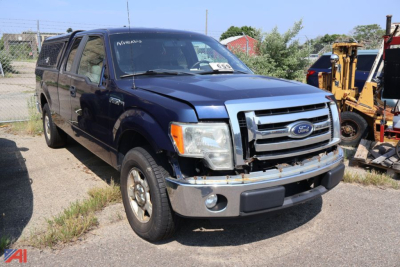 Ford F-150 pickup truck 2013 2WD with blue paint and chrome grille, front bumper, and damaged hood; front-left wheel on gravel lot with equipment in background.