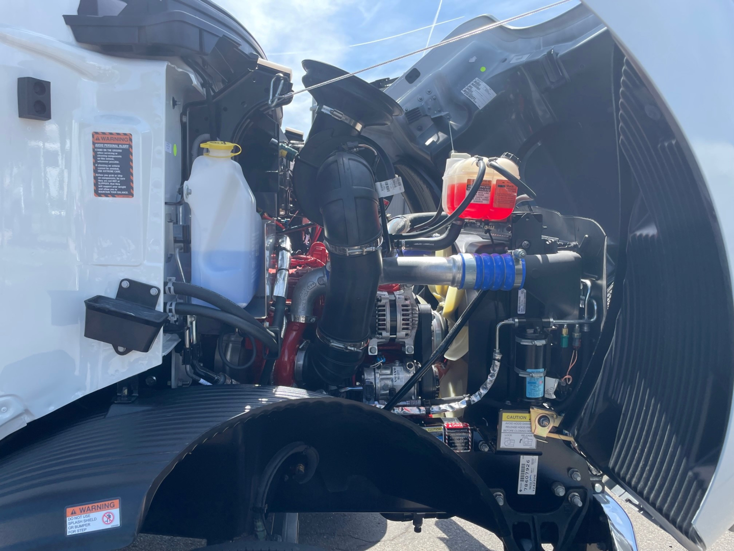 Mack MD6 engine bay showing coolant reservoir, hoses, and engine components in a white cab truck.