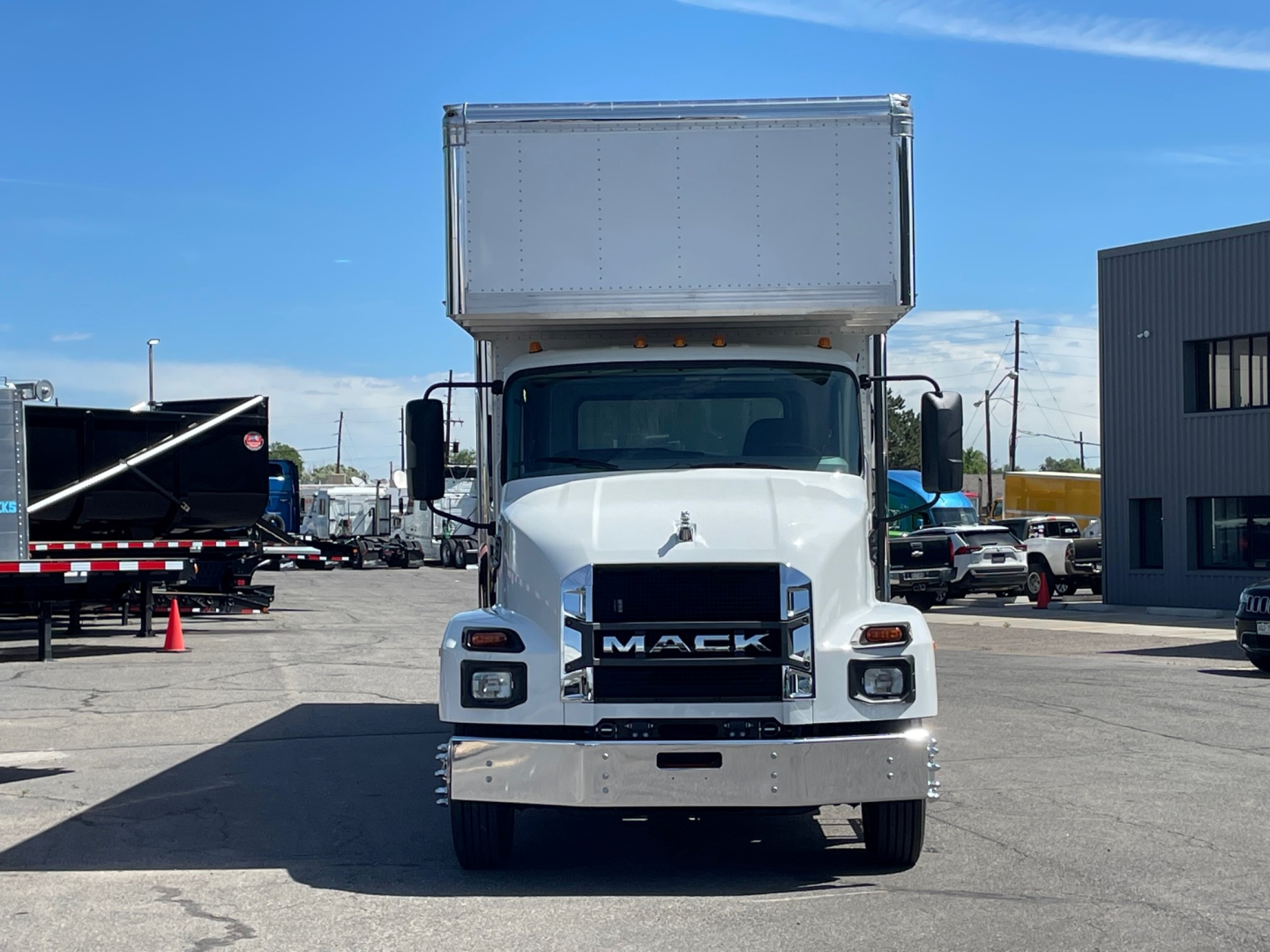 Mack MD6 cab front view showing grille with MACK badge and large white cab, cargo box on top, in a dealership lot.
