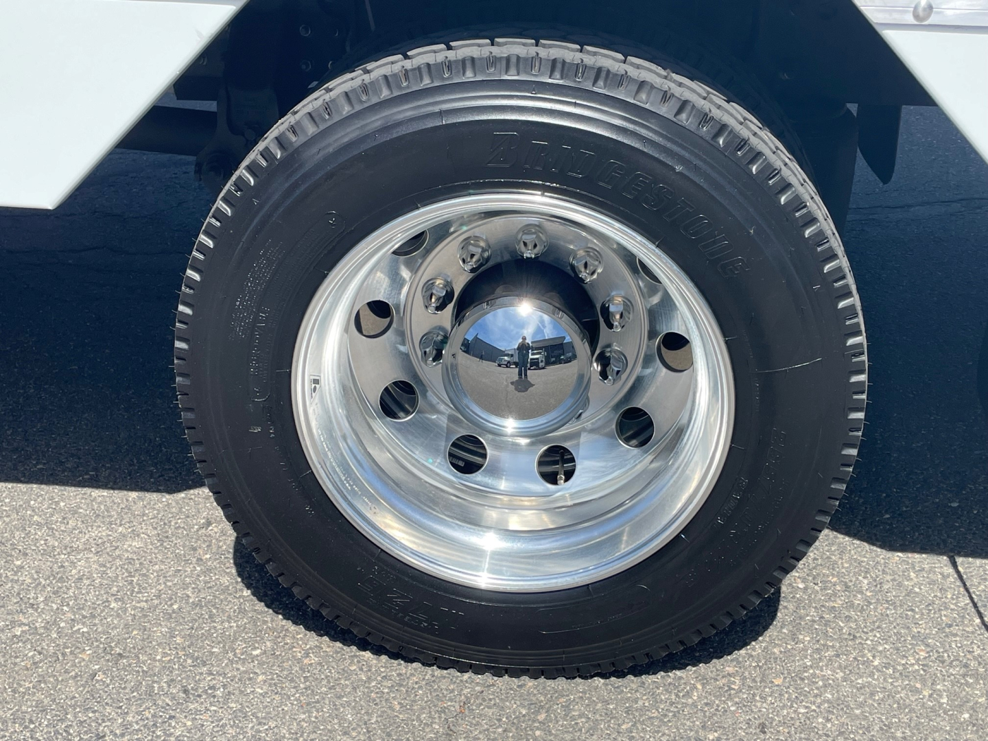 Wheel and tire assembly on a Mack MD6 truck, polished chrome hubcap with multiple lug holes, tire sidewall visible.