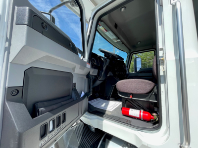 MD6 truck cab interior showing open door and driver's seat with fire extinguisher in the footwell; dashboard and steering wheel visible.