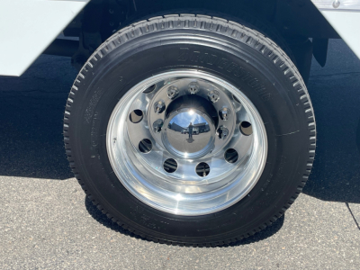 Wheel and tire assembly on a Mack MD6 truck, polished chrome hubcap with multiple lug holes, tire sidewall visible.