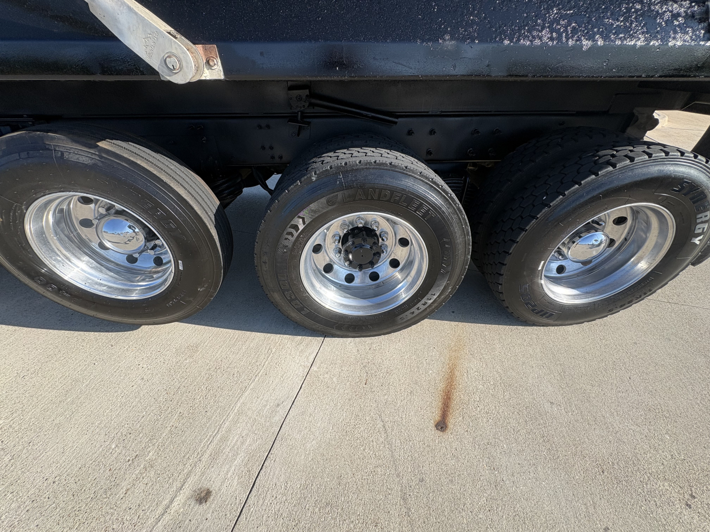 Three axles of a dump truck showing tires and rims with visible wear bands and undercarriage frame. No legible labels or text visible in the image.