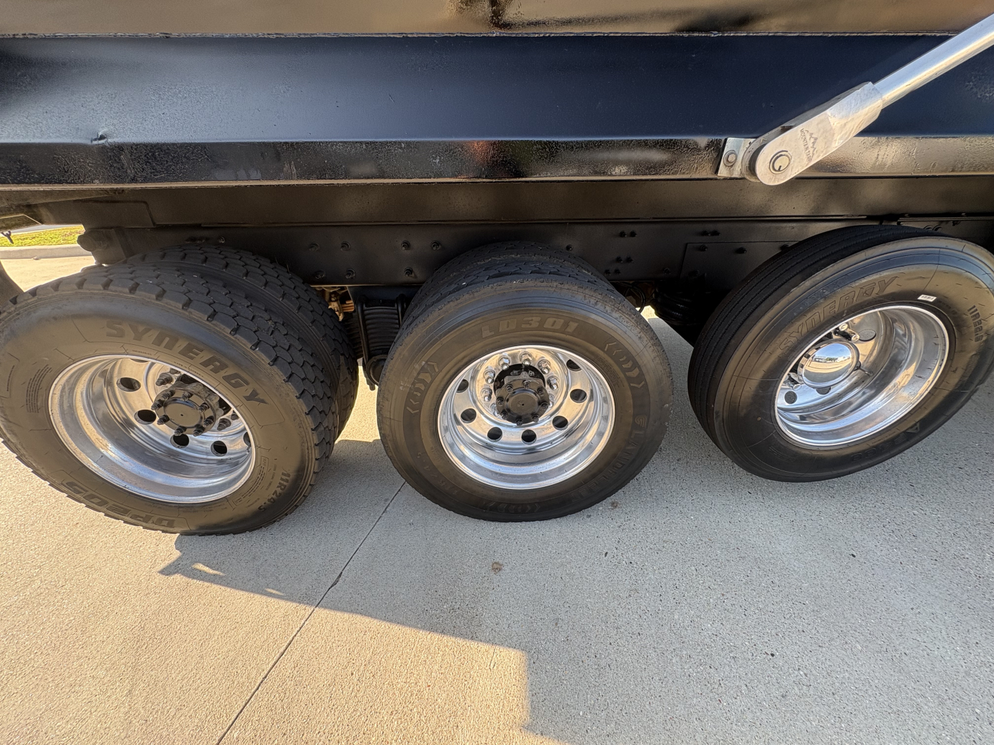 Three axles of a Mack GR64F dump truck showing wheels and tires under the dump bed.