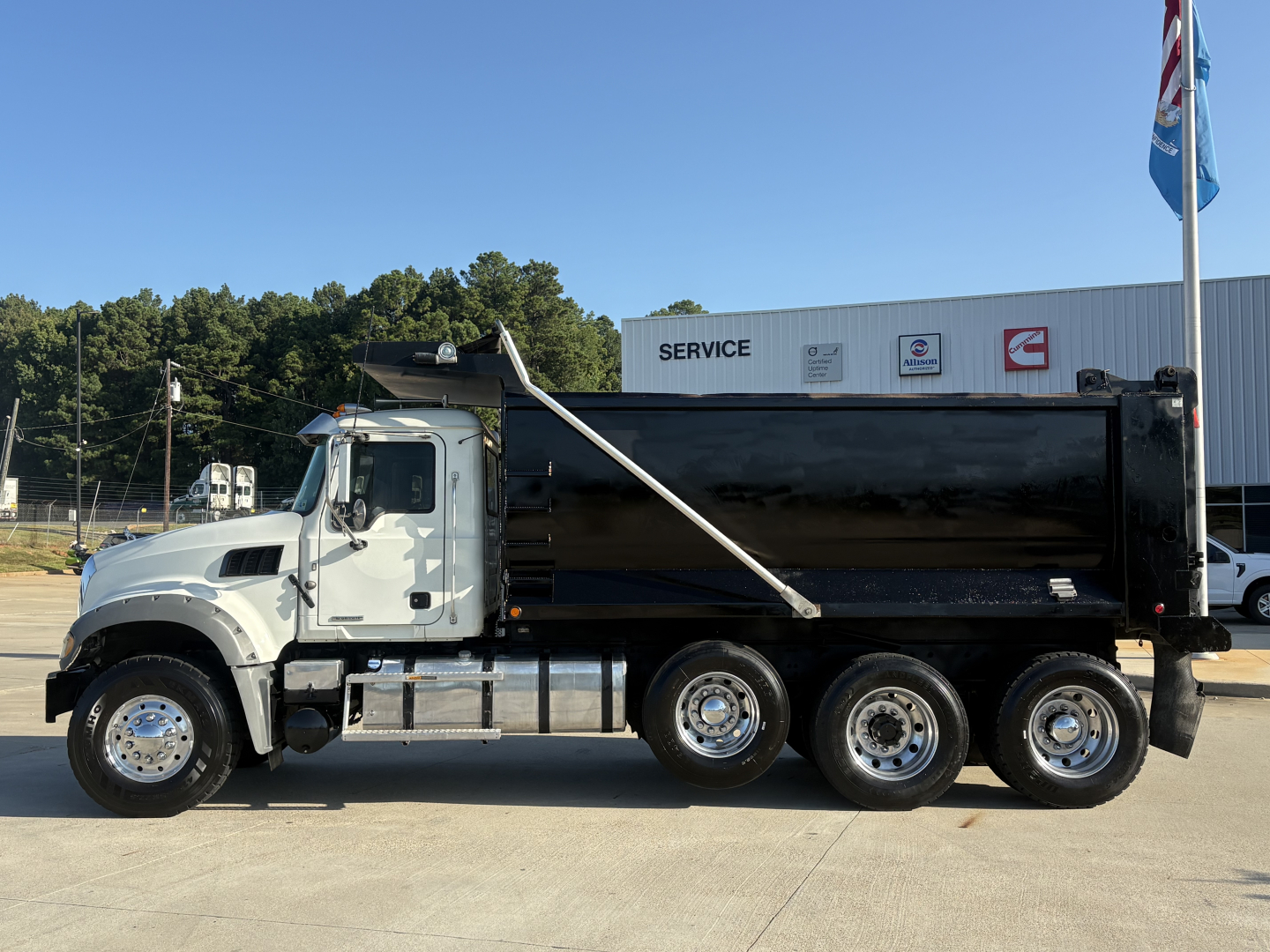 Dump truck side view showing a white cab and black dump body on a Mack GR64F chassis, with six wheels, in-service.