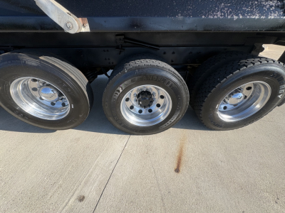 Three axles of a dump truck showing tires and rims with visible wear bands and undercarriage frame. No legible labels or text visible in the image.