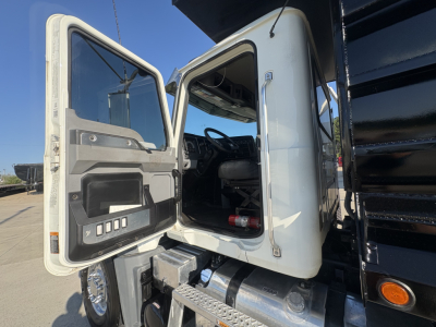 Truck cab interior visible through open driver door on a Mack GR64F dump truck showing steering wheel and dashboard.
