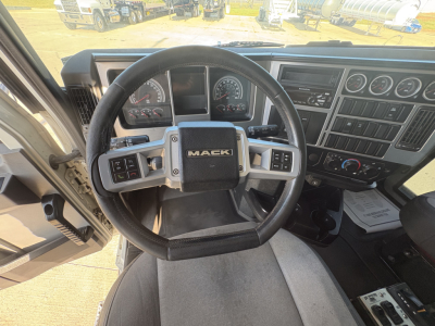 Mack GR64F truck cab interior showing steering wheel with Mack logo and dashboard gauges.