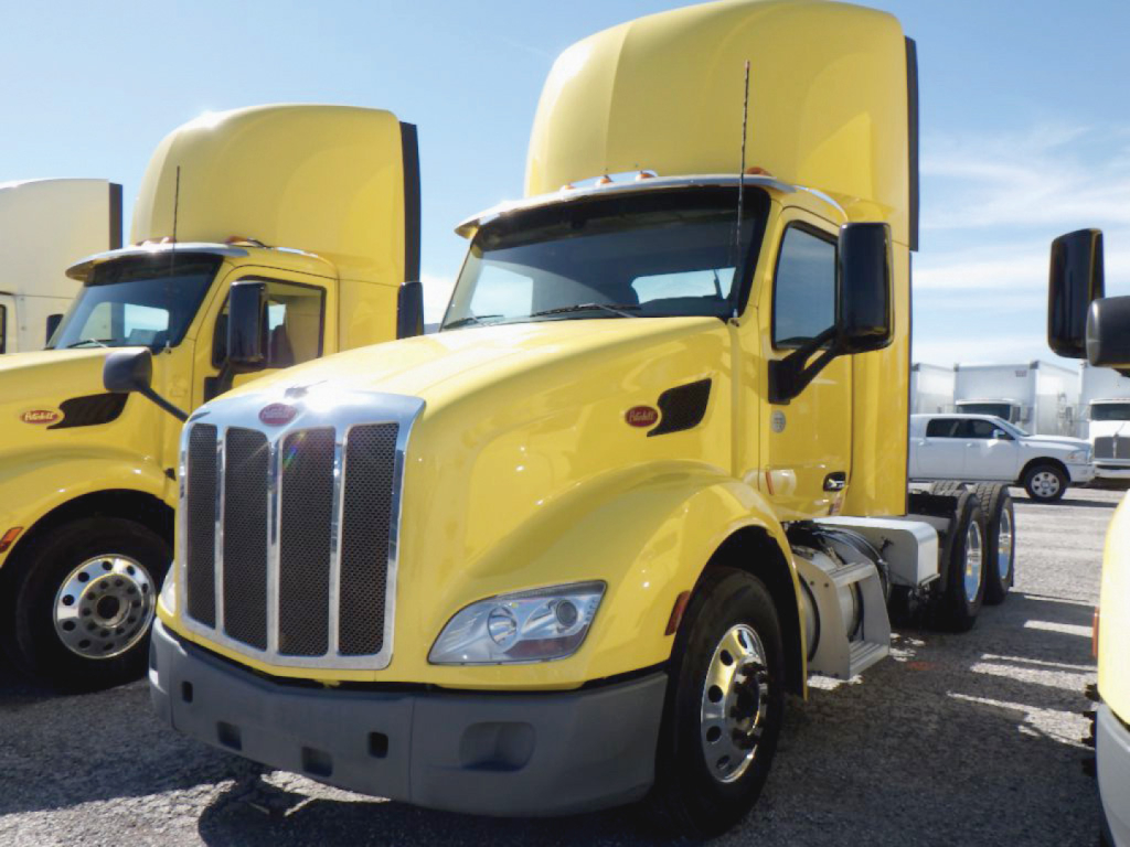 Peterbilt 579 conventional daycab truck in yellow parked with its hood up and another yellow truck nearby