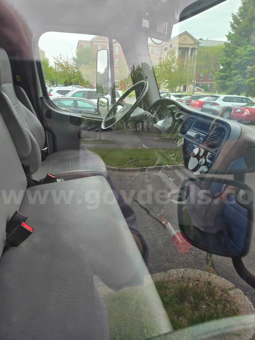 Truck cab interior with steering wheel and dashboard visible through passenger-side window; light reflections on glass.