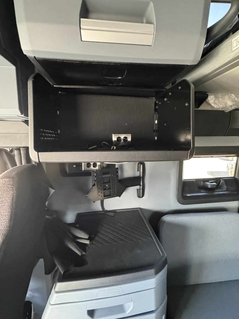 Truck interior: open overhead compartment and dashboard area with mounting hardware and empty tray; visible text not legible.
