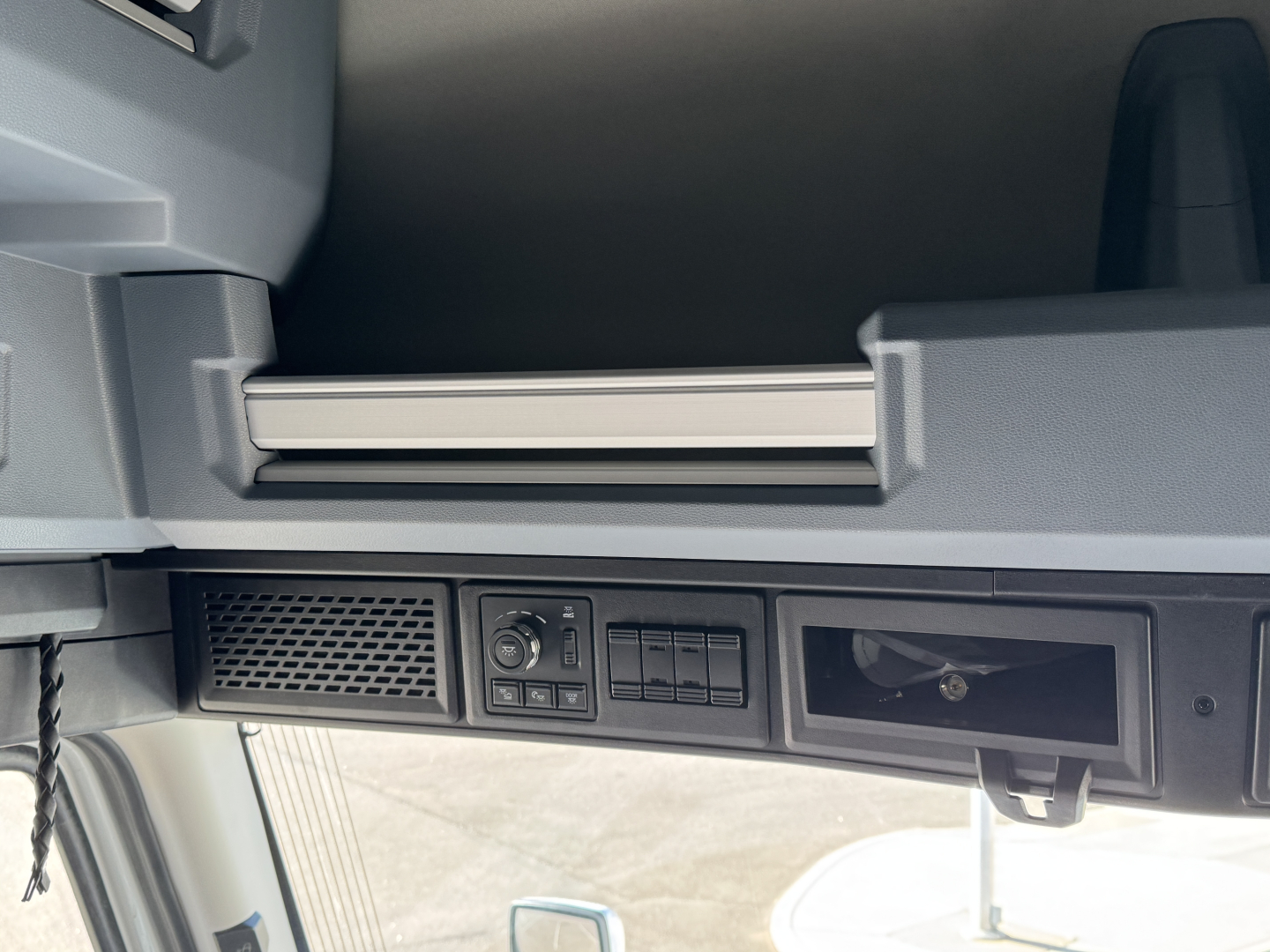 Cab interior dash area of a 2026 Mack PR64T76H showing overhead storage shelf and control panel with vents and empty slot, low lighting