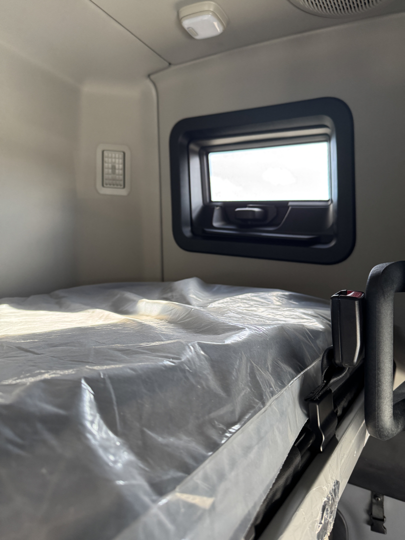 Truck cab interior with sleeper berth covered in protective plastic, window and small vent visible.