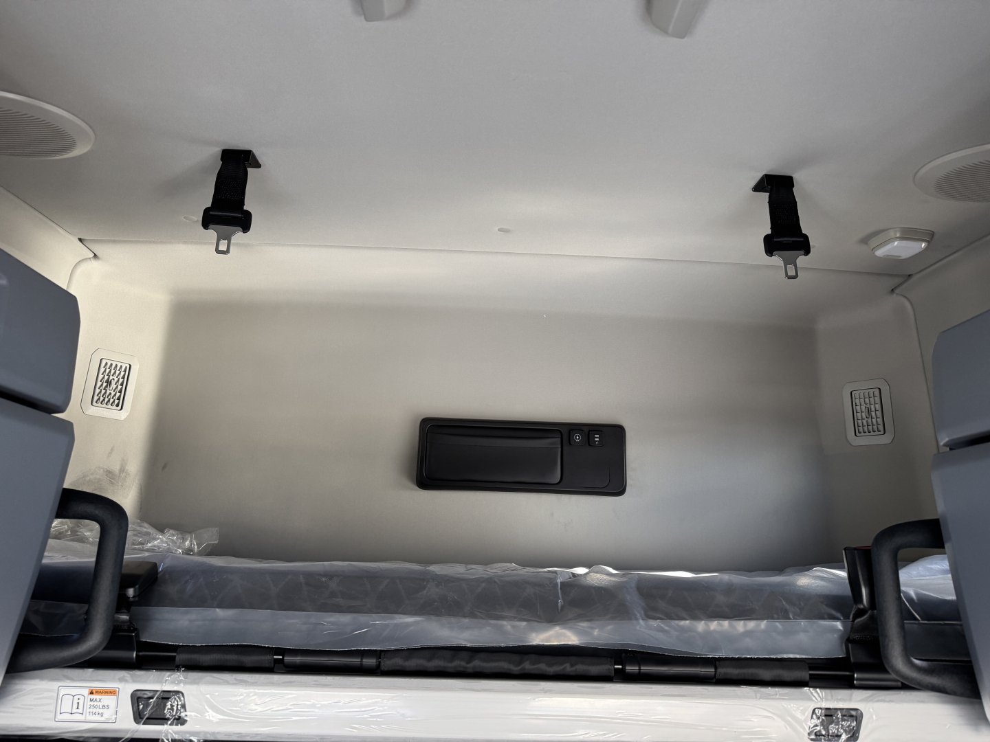 Truck sleeper cab interior showing storage cubby and bench-like bed with metal side panels and electrical panel on the wall.