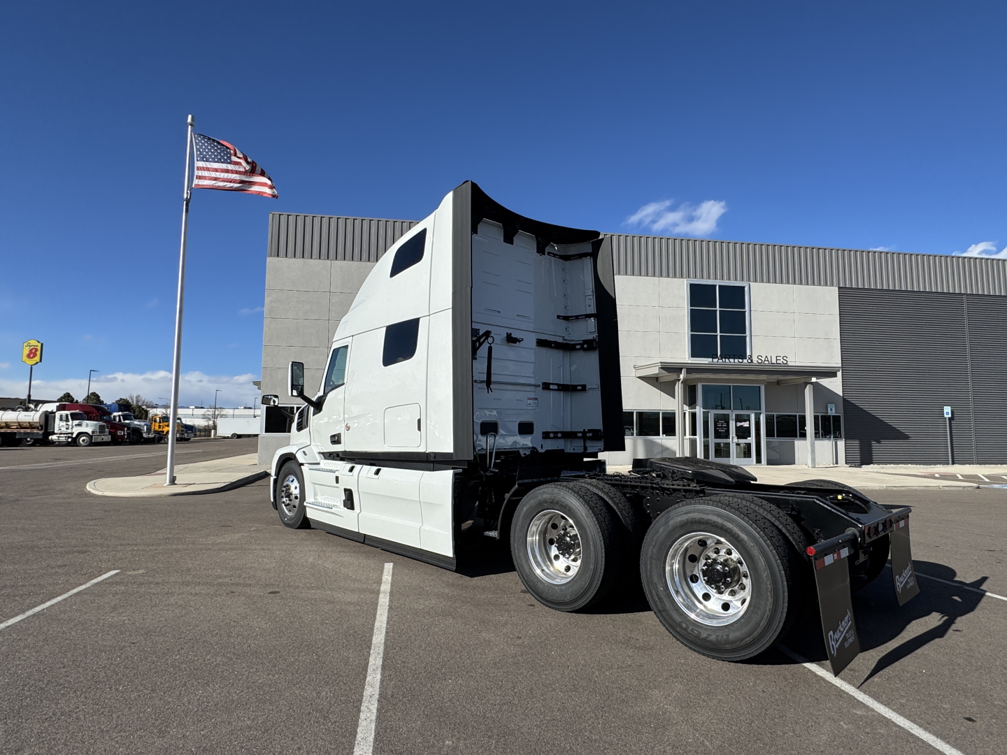 Truck cab and chassis in a dealership lot with American flag; visible text: none clearly legible on vehicle; building in background.