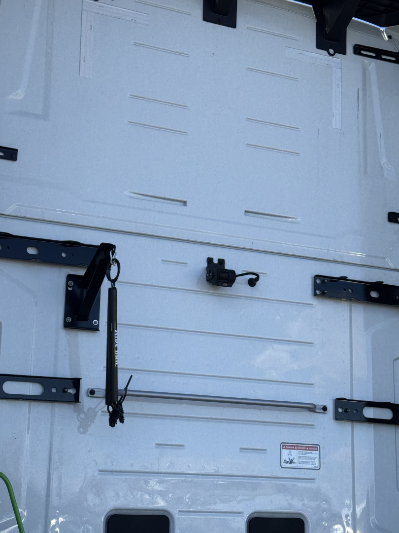 Truck cab interior door area with metal panels and latches showing a small black electrical connector and a long metal rod on a white surface.
