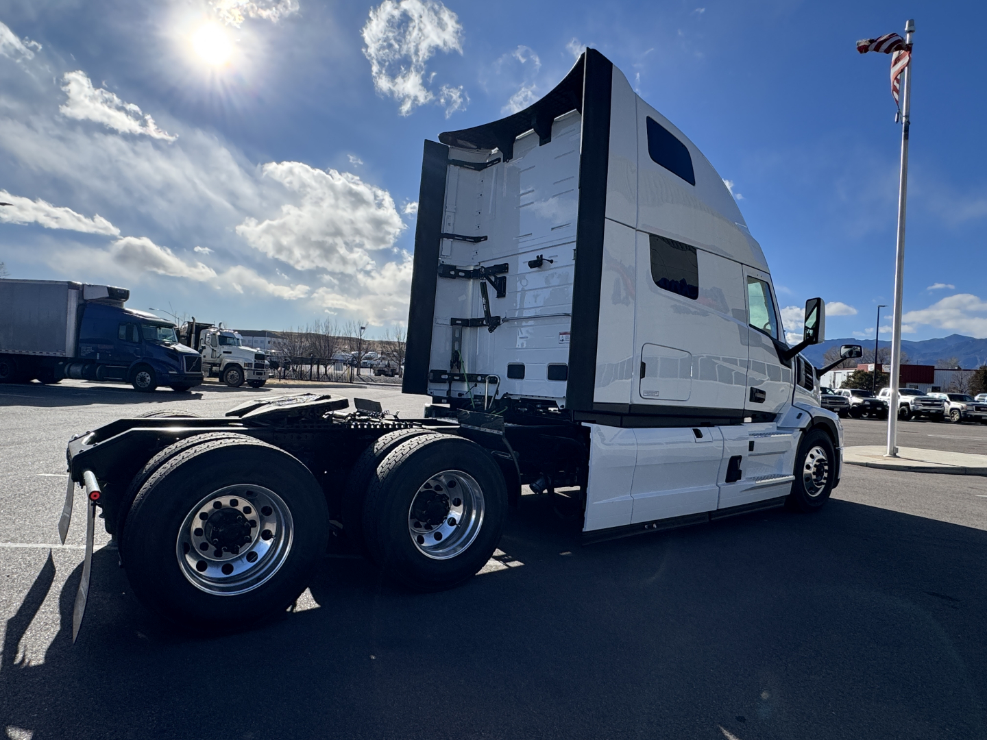 Truck cab and rear dual-axle chassis of a 2026 Mack PR64T76H conventional sleeper, side view, with white cab and black chassis, sunny day.