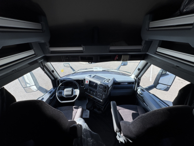 Cockpit view of a Mack PR64T76H truck interior with steering wheel, dashboard, and two front seats visible.