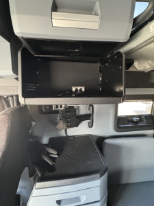 Truck interior: open overhead compartment and dashboard area with mounting hardware and empty tray; visible text not legible.