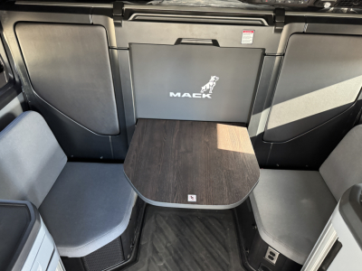 Mack PR64T76H cab interior showing seating area with small wooden table and storage panels.