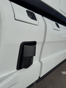 Truck side view showing a black rectangular side marker/wheel well area with white body panels and door outlines.