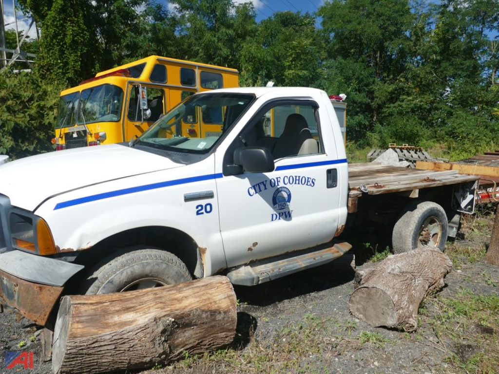Ford F-350 Super Duty pickup with a wooden log bed in a salvage yard, City of Cohoes logo, 4x4, single rear wheel, yellow school bus in background.