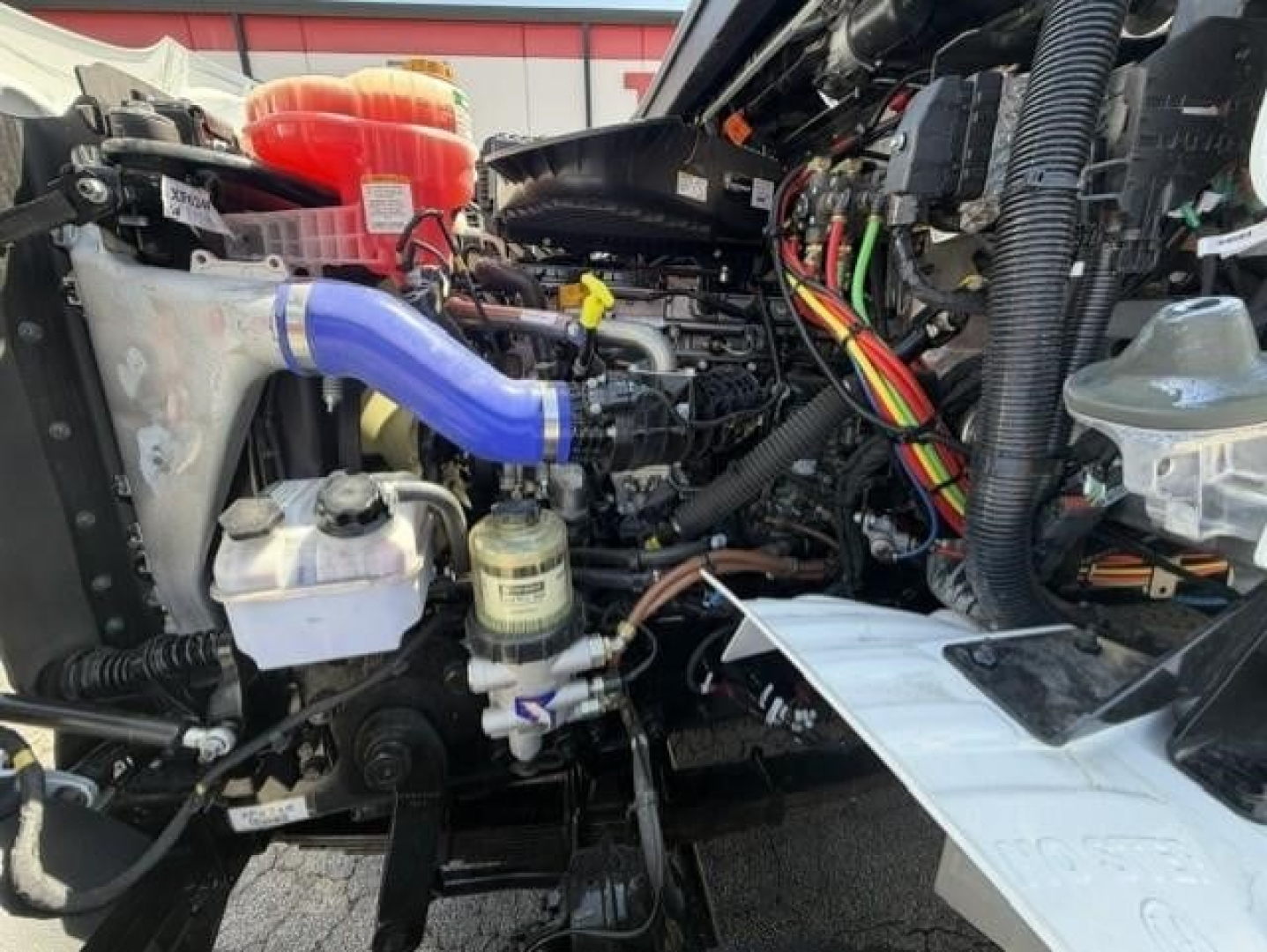 Truck engine bay of a Western Star 47X with components like blue coolant hose, white reservoir, filters, and wiring harnesses visible.