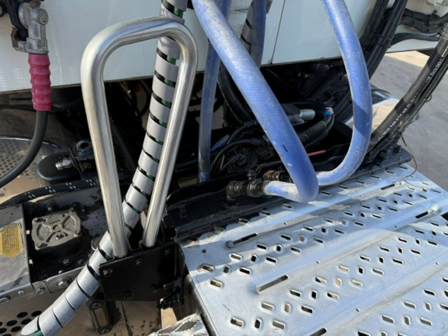 Truck engine bay area showing coolant hoses, metal braided lines, and perforated aluminum step/steps with hoses and wiring visible.