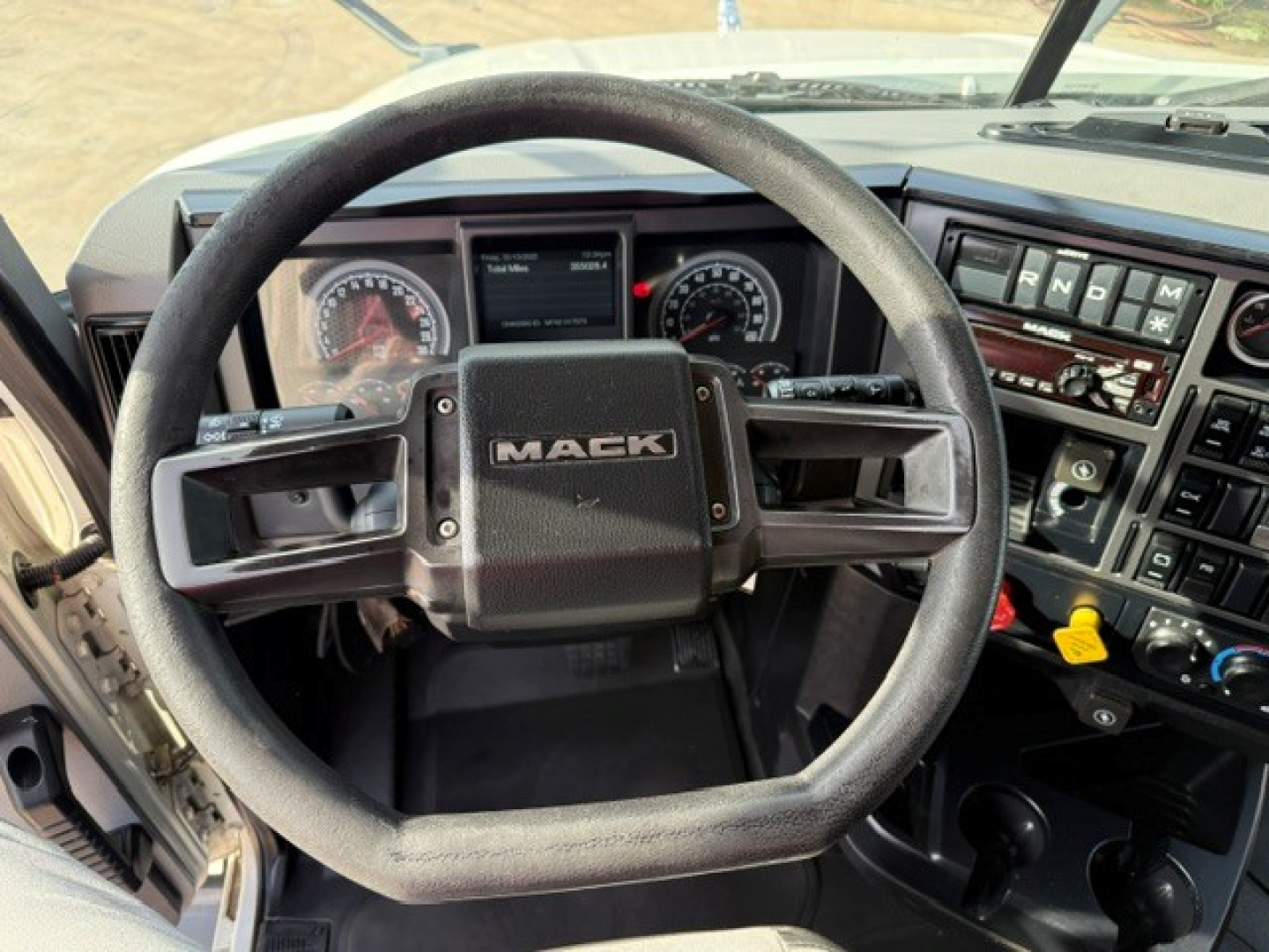 Interior of a Mack truck with steering wheel showing MACK logo, dashboard controls, and gauge cluster visible.