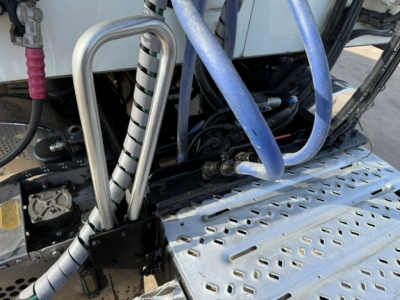 Truck engine bay area showing coolant hoses, metal braided lines, and perforated aluminum step/steps with hoses and wiring visible.