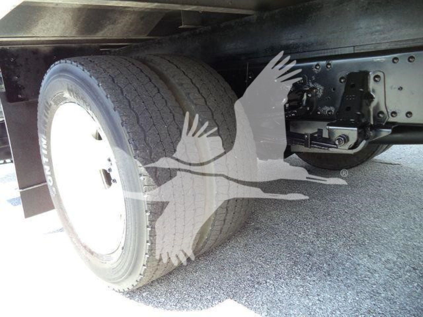 Underneath a box truck showing rear wheel and suspension; no readable text visible other than faint markings on tire sidewall.
