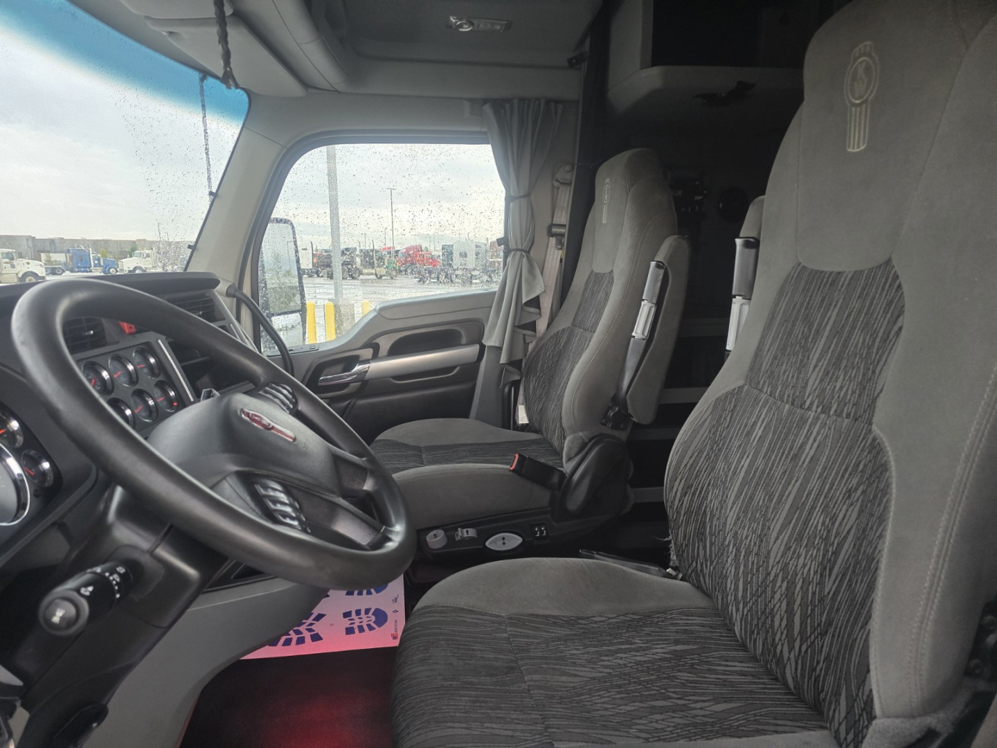 Kenworth T680 truck cabin interior showing driver seat and passenger seat with steering wheel and dashboard visible.