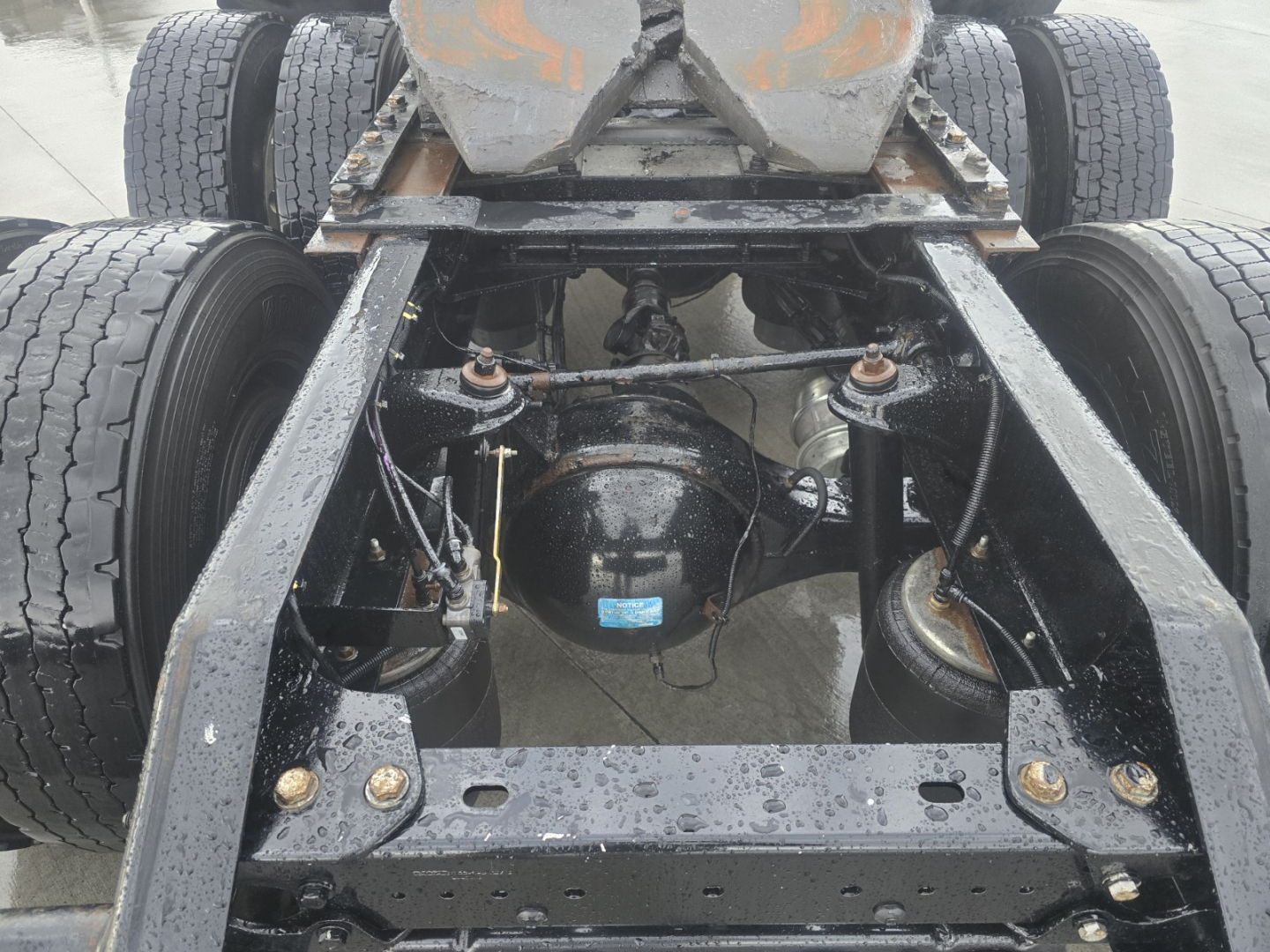 Kenworth T680 chassis view showing rear axle differential and suspension with dual rear wheels and visible frame rails; some components and hoses visible.