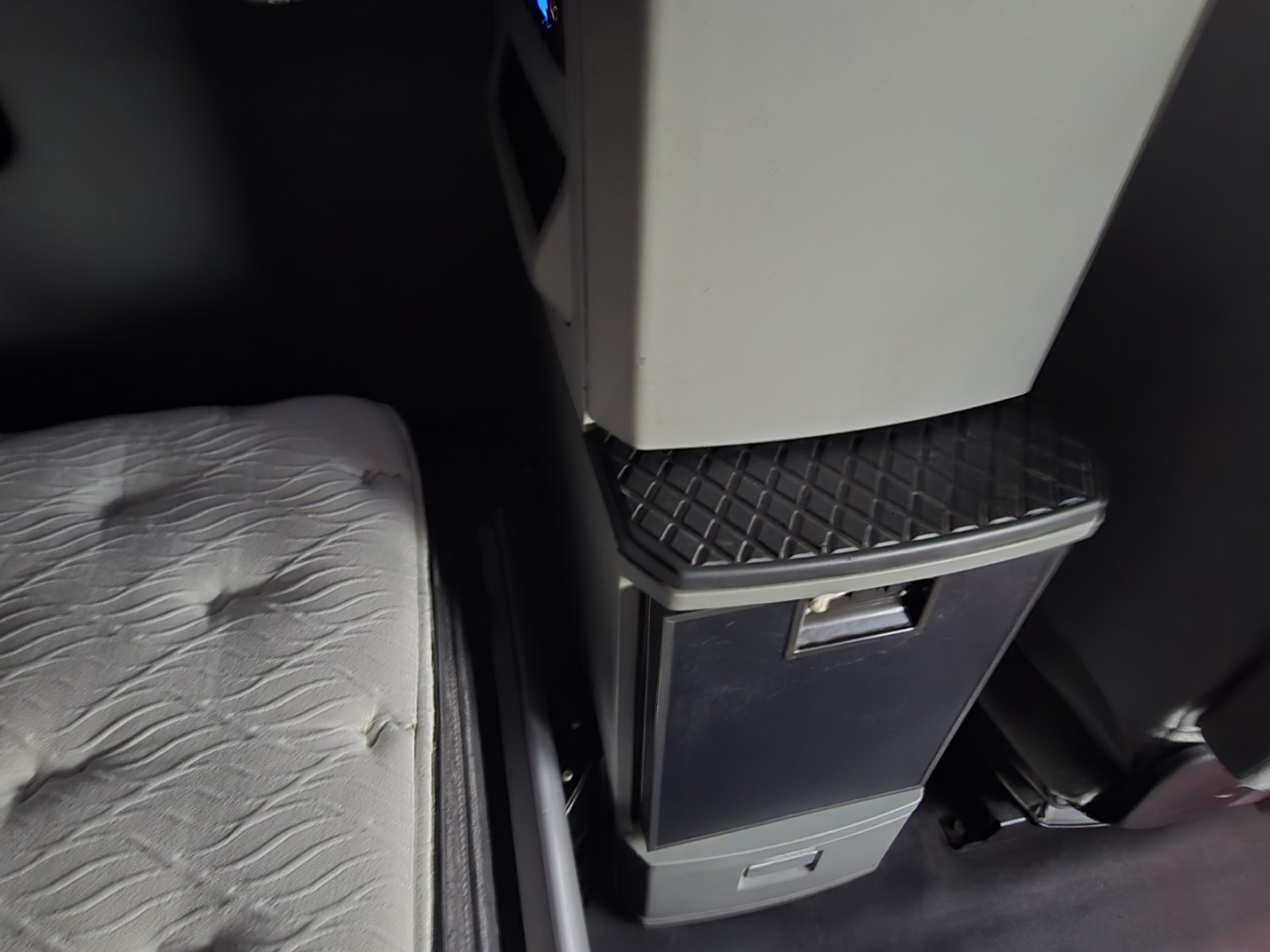 Cab interior of a Kenworth truck showing a vertical storage cabinet with a small handle and a lower drawer, plus part of a cushioned seat edge.