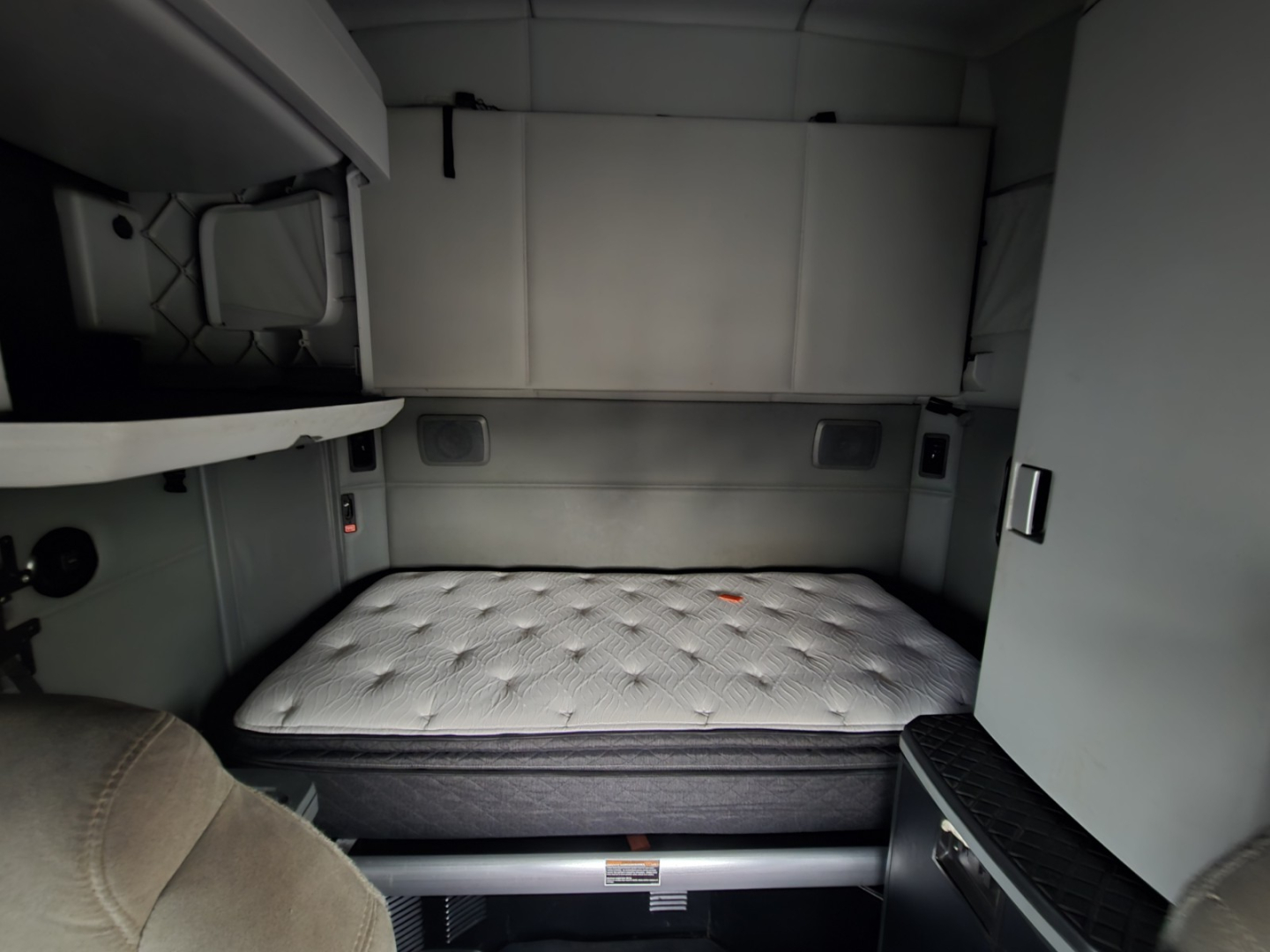 Cab interior of a Kenworth T680 sleeper showing a bed with mattress and side cabinets.