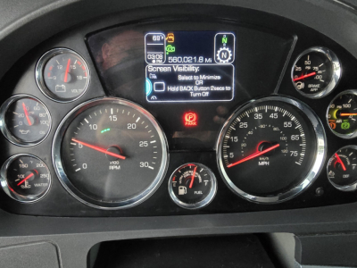Dashboard of a Kenworth T680 showing multiple gauges, center digital display, and warning icons.