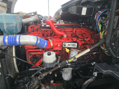 Kenworth T680 engine bay showing Cummins ISX 15 red diesel engine with blue coolant hose, various wiring, and fluid reservoirs.