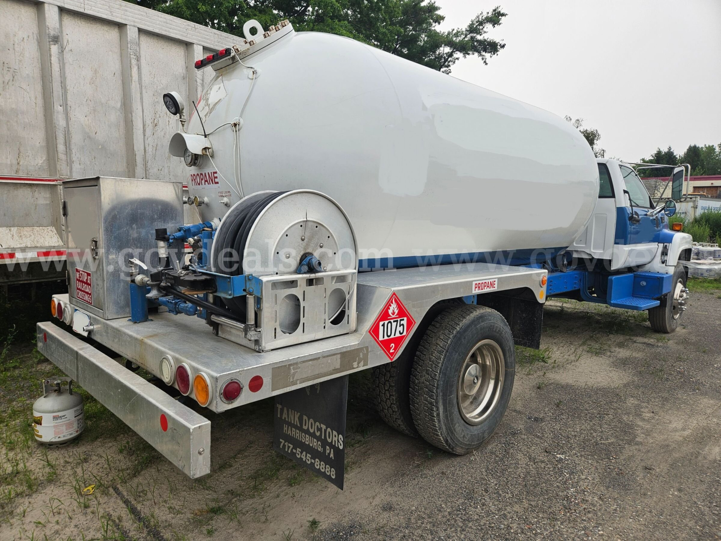 GMC tank truck with cylindrical tank mounted on chassis showing rear hazard placard 1075 and tank access fittings.