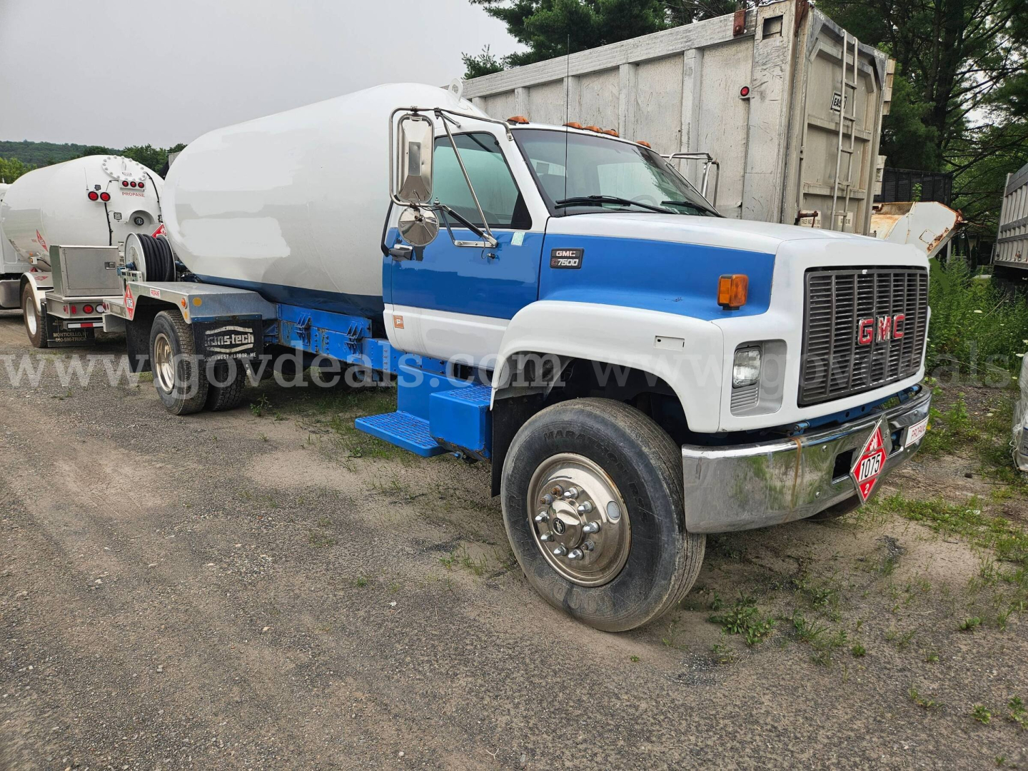 GMC C7500 truck with white cab and blue bumper showing a large white tank trailer