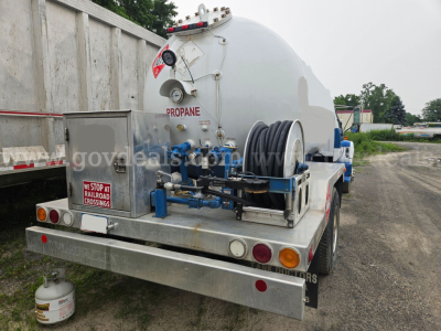 Tank truck rear view showing propane tank with hoses and reels, rear bumper, and hazard labels on tank.