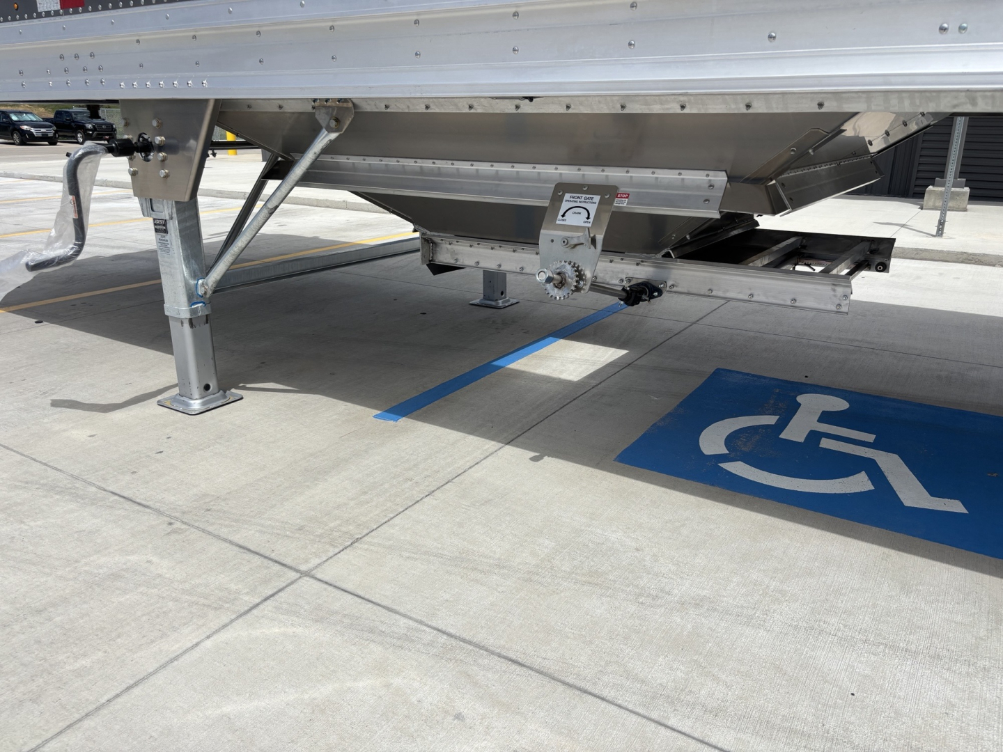 Trailer leg and undercarriage of a Stoughton 40' aluminum grain hopper showing wheel chock and support leg near a handicap parking space.
