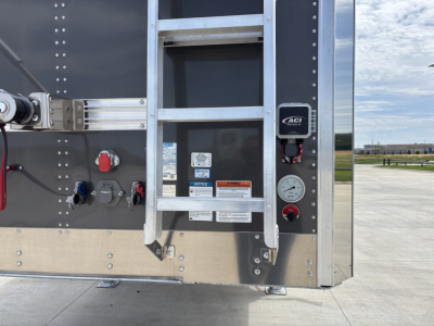 Ladder and control panel on Stoughton grain hopper trailer rear corner with gauges, labels, and ladder rungs visible.