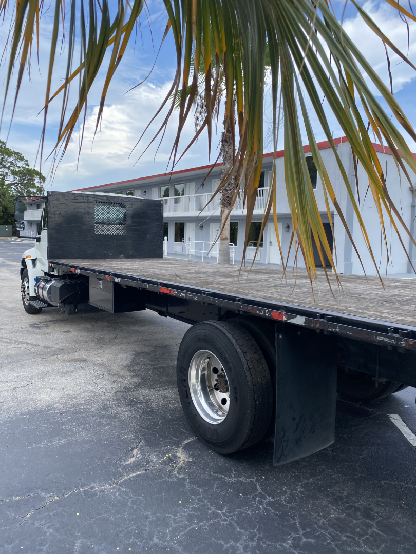 Flatbed truck with extended aluminum deck and dual rear wheels, International 4300, black splitter shield at cab, white cab, in a parking lot.