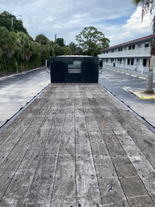 Flatbed truck bed of a 2018 International 4300 with wooden deck and metal cab front seen from rear, construction vehicle dimensions.