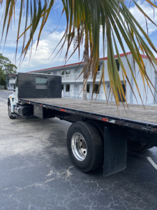 Flatbed truck with extended aluminum deck and dual rear wheels, International 4300, black splitter shield at cab, white cab, in a parking lot.